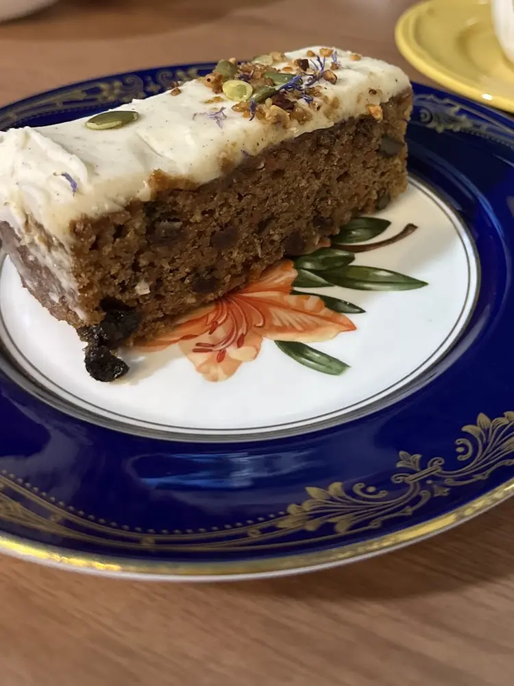 Carrot cake slice on an ornate blue and gold plate with a teapot behind
